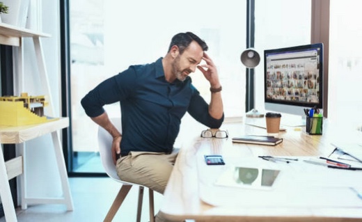 a man sitting at a desk with chronic back pain who needs chiropractic care